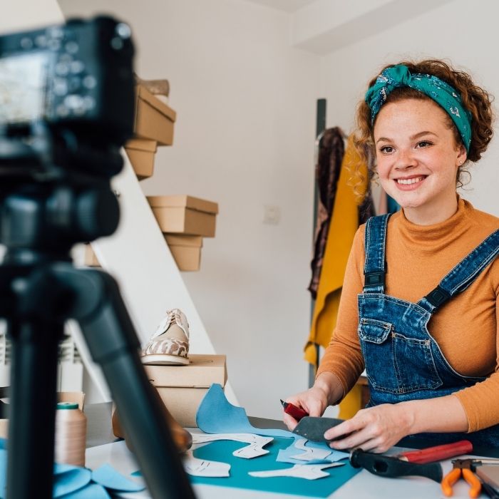 woman cutting cloth, smiling and filming on a camera
